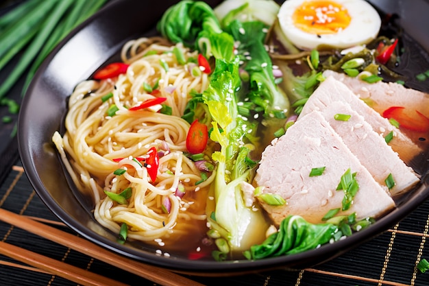 Miso Ramen Azjatycki makaron z jajkiem, wieprzowiną i kapustą pak choi w misce na ciemnej powierzchni.