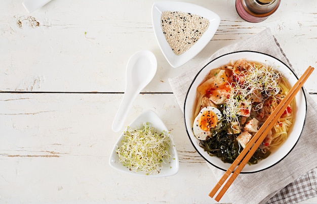 Miso Ramen Azjatycki makaron z kimchi kapustą, wodorostami, jajkiem, pieczarkami i tofu z serem w misce na białym drewnianym stole.