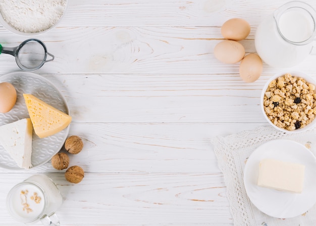 Mleko; jajka; miska płatków zbożowych; ser; mąka i orzechy włoscy na białym drewnianym stole