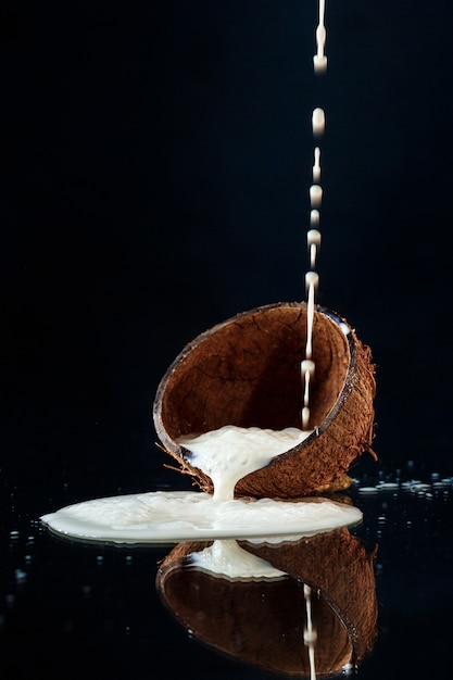 Bezpłatne zdjęcie mleko leje się w połowie kokosa na czarnej ścianie