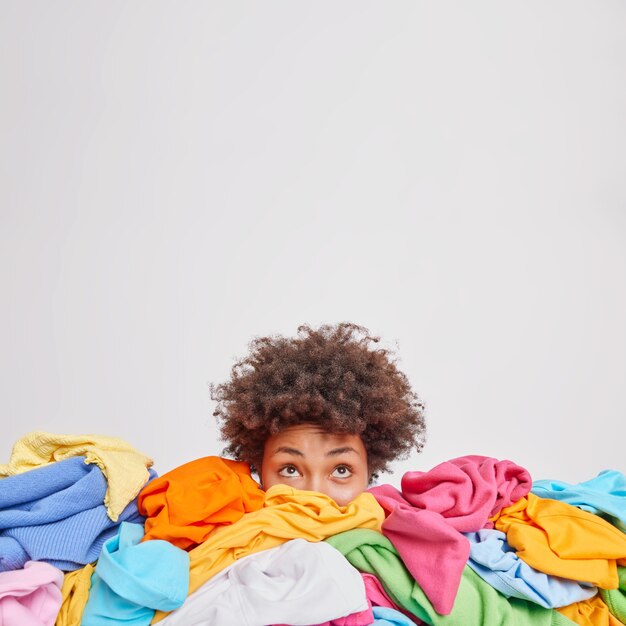 Młoda Afroamerykanka otoczona różnymi kolorowymi ubraniami sortuje garderobę skupioną nad odizolowaną nad białą ścianą pustą przestrzenią na Twoje treści reklamowe. Nic do noszenia koncepcji