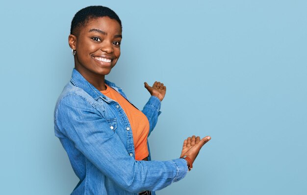 Młoda Afroamerykanka ubrana w zwykłe ubrania zapraszająca do wejścia uśmiechnięta naturalnie z otwartą dłonią