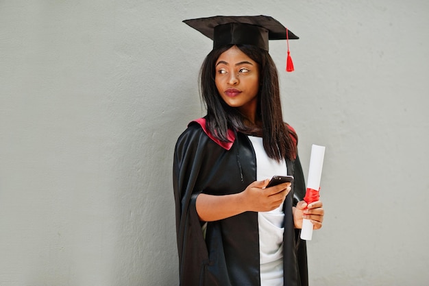 Bezpłatne zdjęcie młoda afroamerykańska studentka z dyplomem i telefonem komórkowym pozuje na zewnątrzxa