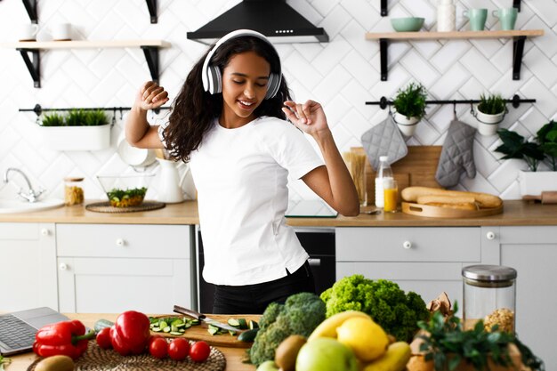 Młoda afrykańska kobieta tańczy i słucha muzyki przez słuchawki w kuchni