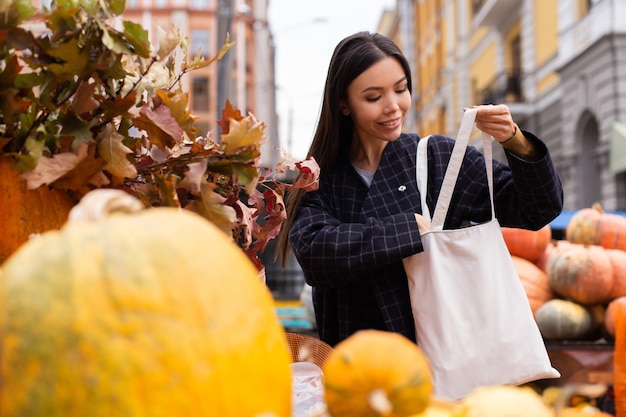 Młoda atrakcyjna dorywcza kobieta szczęśliwie kupuje dynię w jesiennym sklepie rolniczym na świeżym powietrzu