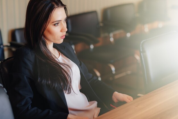 Młoda atrakcyjna dziewczyna emocjonalne w ubrania w stylu biznesowym, siedząc przy biurku z telefonem w biurze lub publiczności