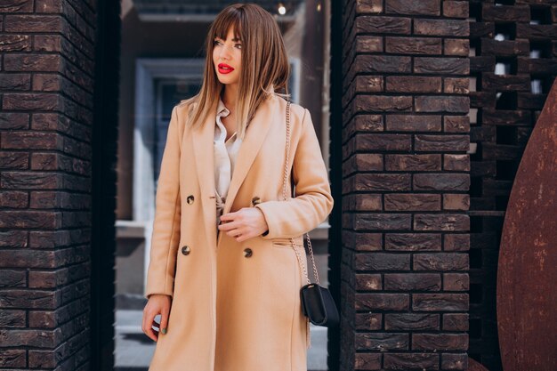 Młoda atrakcyjna kobieta w beżowym płaszczu pozuje na ulicy