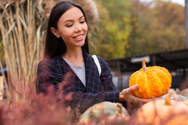 Młoda atrakcyjna przypadkowa kobieta z radością kupująca dynię na dzień Halloween w jesiennym sklepie rolniczym na świeżym powietrzu