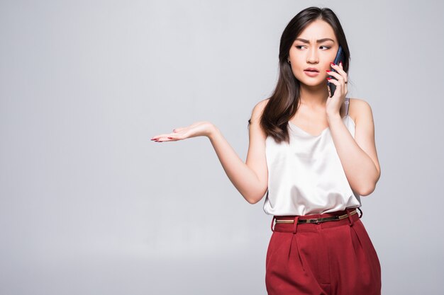 Młoda Azjatycka dziewczyna na telefonie odizolowywającym na biel ścianie