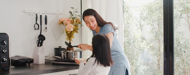 Młoda Azjatycka Japońska mama i córka gotuje w domu. Styl życia kobiety szczęśliwe robi makaronowi i spaghetti wpólnie dla śniadaniowego posiłku w nowożytnej kuchni przy domem w ranku.