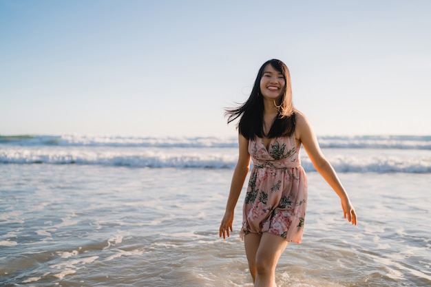 Młoda Azjatycka kobieta chodzi na plaży. Piękny żeński szczęśliwy relaksuje chodzić na plaży blisko morza gdy zmierzch w wieczór.
