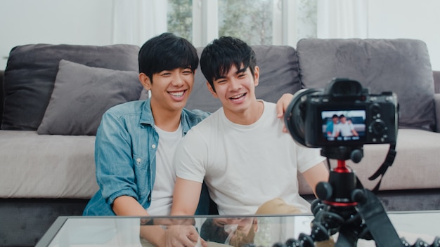 Młoda Azjatycka para gejów influencer para vlog w domu. Nastoletni koreańscy mężczyźni LGBTQ szczęśliwi relaksują się przy użyciu kamery zapisującej vlog wideo w mediach społecznościowych, leżąc na kanapie w salonie w domu.