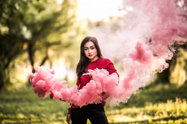 Młoda azjatykcia kobieta trzyma czerwoną kolorową dymną bombę na plenerowym parku. Czerwony dym rozprzestrzenia się na festiwalu cerebracji.