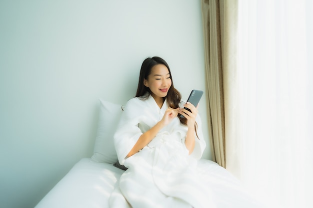Młoda azjatykcia kobieta używa mobilnego mądrze telefon na łóżku