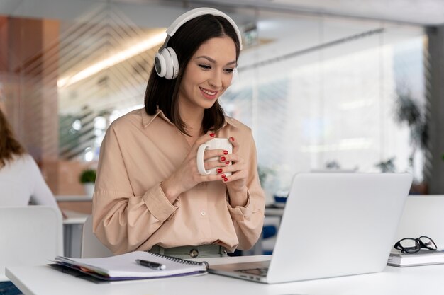 Młoda biznesowa kobieta pracująca w biurze z laptopem i słuchawkami