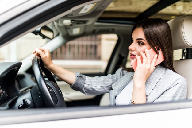 Młoda biznesowa kobieta za pomocą swojego telefonu podczas prowadzenia samochodu