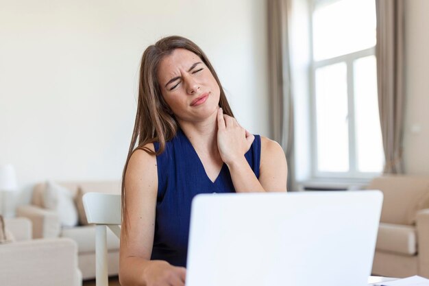 Młoda bizneswoman cierpi na ból szyi, masując szyję, siedząc w swoim miejscu pracy w domowym biurze