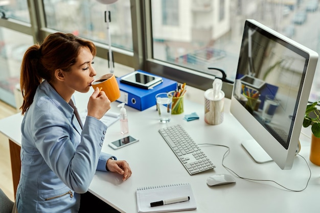Młoda bizneswoman pije kawę z zamkniętymi oczami podczas przerwy w pracy w biurze