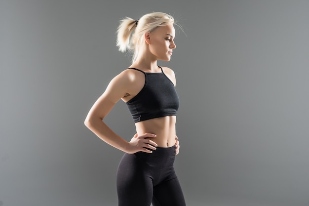 Młoda blondynka dopasowana sportowa dziewczyna kobieta w czarnej odzieży sportowej demonstruje jej silne muskularne ciało rozciągające się