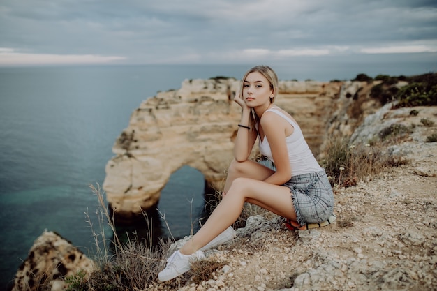 Młoda Blondynka Kobieta Siedzi Na Szczycie Skały Nad Oceanem.