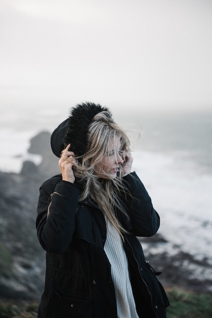 Młoda blondynka w kapeluszu chodzenie po skalistym wybrzeżu w wietrzną pogodę