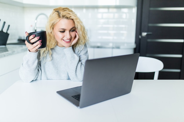 Bezpłatne zdjęcie młoda blondynki kobieta używa laptop w kuchni w domu