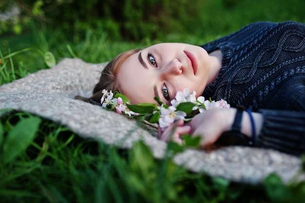 Młoda brunetka dziewczyna leżąca na zielonej trawie z gałęziami kwitnącego drzewa