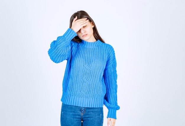 Młoda brunetka dziewczyna w niebieskim swetrze o ból głowy na białym.