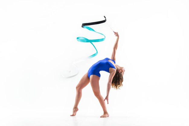 Młoda brunetka kobieta gimnastyczka ćwiczy kalisteniki z niebieską wstążką