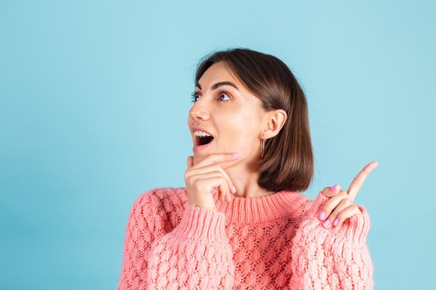 Młoda brunetka w ciepły różowy sweter na białym tle na niebieskiej ścianie