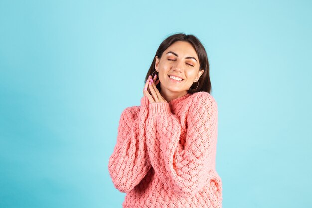 Młoda brunetka w różowym swetrze na białym tle na niebieskiej ścianie