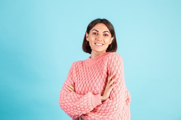 Młoda brunetka w różowym swetrze na białym tle na niebieskiej ścianie