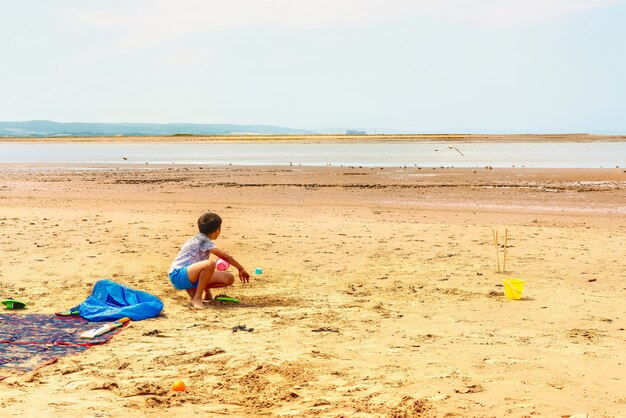 Młoda chłopiec bawić się z piaskiem na plaży na słonecznym dniu