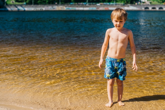 Młoda chłopiec w skrótach stoi na dennej plaży