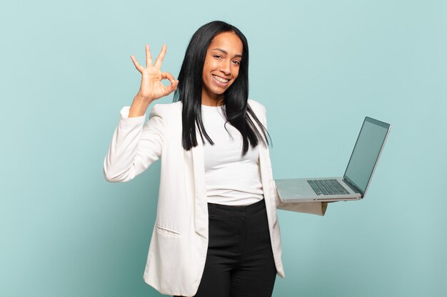 Młoda czarna kobieta czuje się szczęśliwa, zrelaksowana i zadowolona, okazując aprobatę dobrym gestem, uśmiechając się. koncepcja laptopa