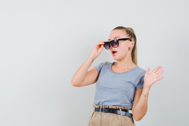 Młoda dama patrząc przez okulary i macha ręką w t-shirt i spodnie