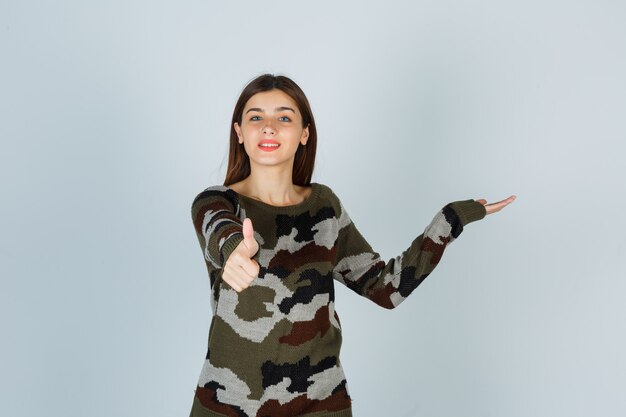 Młoda Dama Pokazuje Kciuk W Górę, Udając, że Pokazuje Coś W Swetrze