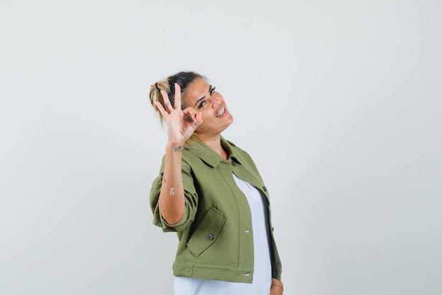 Bezpłatne zdjęcie młoda dama pokazuje ok gest w kurtce t-shirt i patrząc wesoło