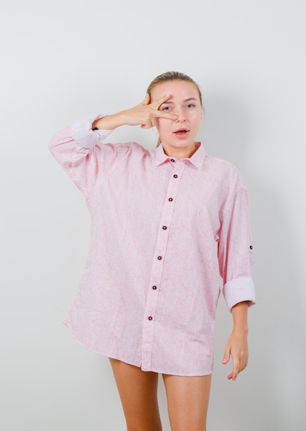 Bezpłatne zdjęcie młoda dama pokazuje znak v na oku w różowej koszuli i wygląda ładnie