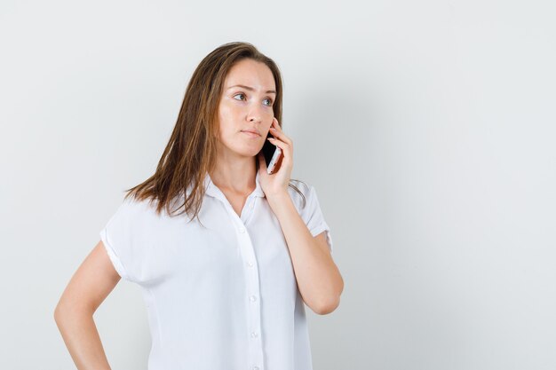 Młoda dama rozmawia przez telefon w białej bluzce i wygląda na zrelaksowaną