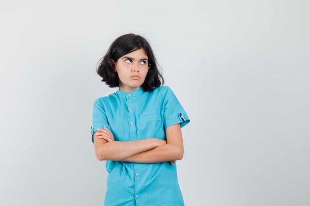 Młoda dama stojąca ze skrzyżowanymi rękami, patrząc w górę w niebieskiej koszuli i wyglądająca na obrażoną.