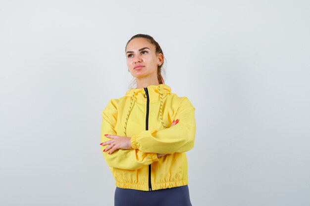 Młoda dama stojąca ze skrzyżowanymi rękami w żółtej kurtce i zamyślona. przedni widok.