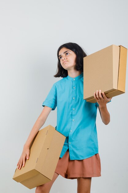 Młoda dama trzyma pudełka w niebieskiej koszuli i szuka gotowy.