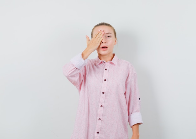 Młoda dama trzymając rękę na oku w różowej koszuli