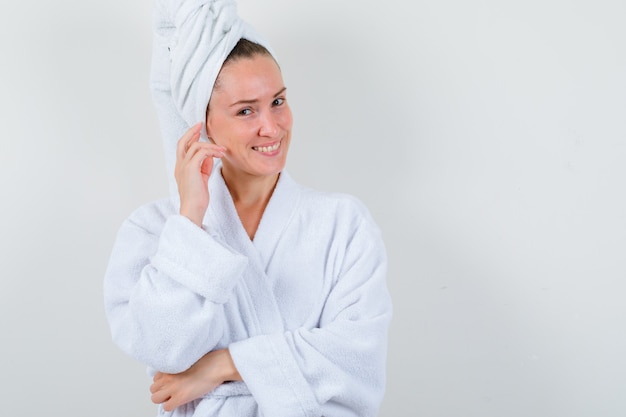Młoda dama w białym szlafroku, ręcznik trzymając rękę na głowie i patrząc radośnie, widok z przodu.