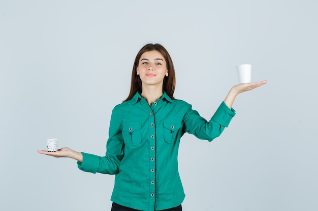 Młoda dama w koszuli, trzymając plastikowe filiżanki kawy i patrząc zadowolony, widok z przodu.
