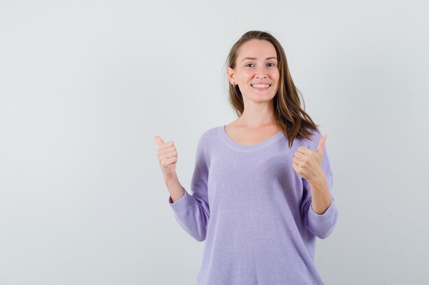 Młoda dama w przypadkowej koszuli pokazuje podwójne kciuki i wygląda na szczęśliwego