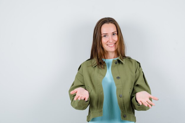 Młoda dama w t-shirt, kurtka rozłożyła dłonie, patrząc w kamerę i patrząc na szczęśliwego, widok z przodu.