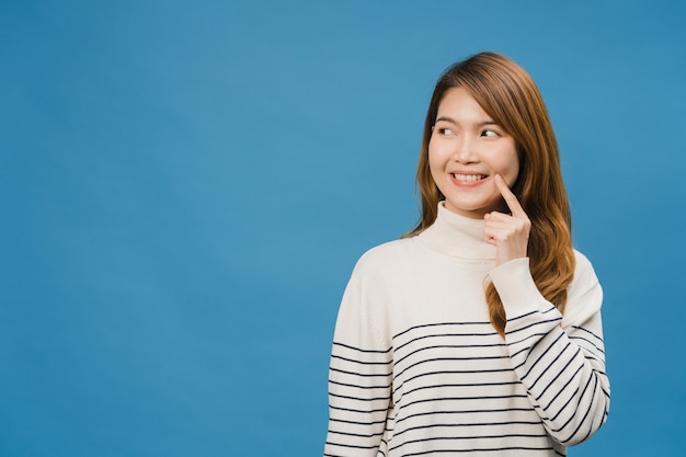 Bezpłatne zdjęcie młoda dama z azji pokazująca uśmiech, pozytywną ekspresję, ubrana w zwykłą odzież i zabawne uczucie odizolowane na niebieskiej ścianie
