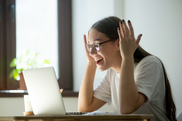 Młoda dorosła kobieta otrzymywa dobre dobre wieści przez jej laptopu